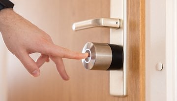 Une main s'apprête à toucher un Nuki Smart Lock Pro sur une porte.