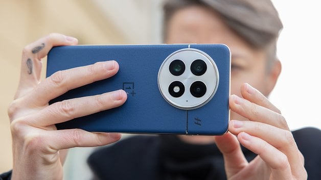 A person holding a blue OnePlus 13 smartphone with three rear cameras, focused on taking a photo.