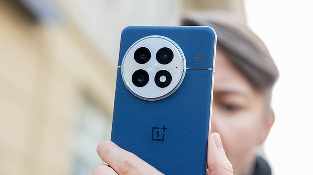 A person holding the blue back of a OnePlus 13 smartphone, showcasing its camera design.