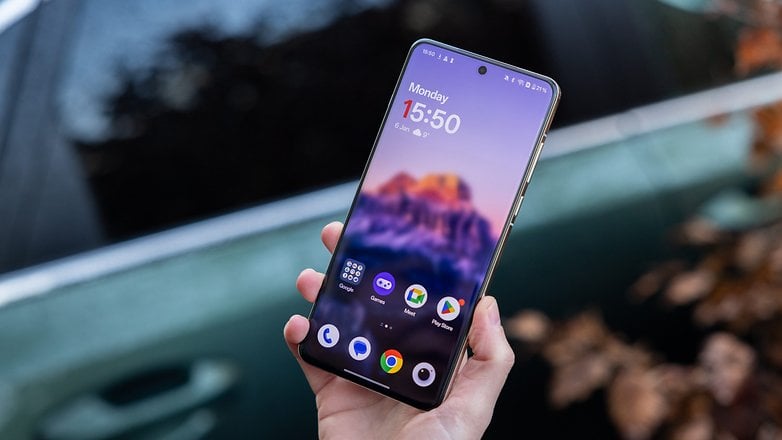 A person holding a OnePlus 13 smartphone with a colorful home screen showing the time 15:50.