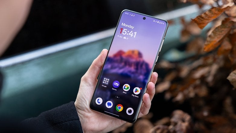 Uma pessoa segurando um smartphone OnePlus 13 exibindo a tela inicial com hora e aplicativos. Uma pessoa segurando um smartphone OnePlus 13 exibindo a tela inicial com hora e aplicativos.