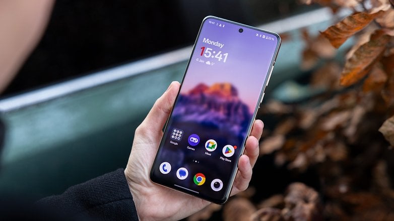 En person som håller en OnePlus 13-smarttelefon som visar startskärmen med tid och appar.