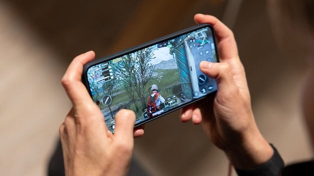 A person gaming on a OnePlus 13 smartphone, showing a battle scene on the screen.