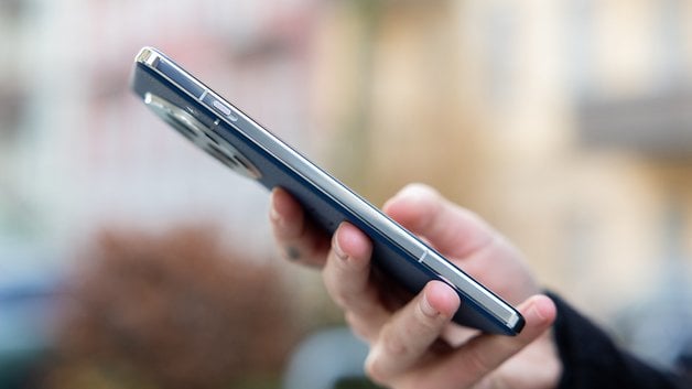 A person holding a OnePlus 13 smartphone, showing its sleek side profile.