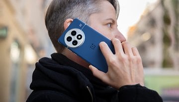 A person with short gray hair is using a OnePlus 13 phone while talking on the street.