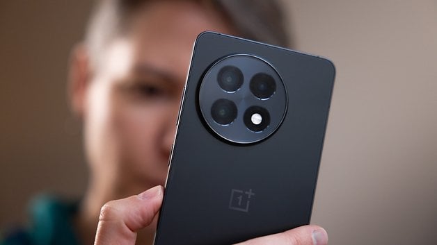 A close-up of a OnePlus 13R smartphone being held by a person, showing its rear camera design.