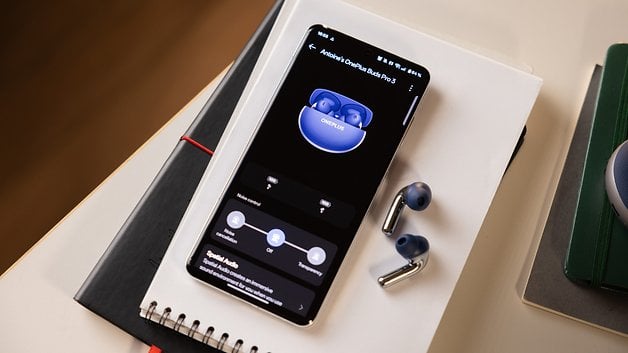 Un smartphone affichant les paramètres des OnePlus Buds Pro 3, avec les écouteurs posés sur un carnet.