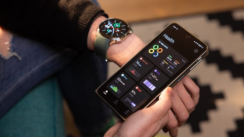 La OnePlus Watch 2 portée à un poignet gauche tandis qu'une main droite tient le OnePlus 12 avec l'application OHealth ouverte