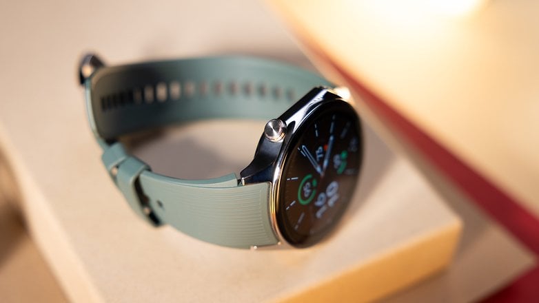 Montre OnePlus 2 avec un bracelet vert, affichant différents cadrans sur une surface.