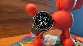 La OnePlus Watch 2R vue de de face avec son écran allumé et posée diagonalement contre une petite statuette rouge.