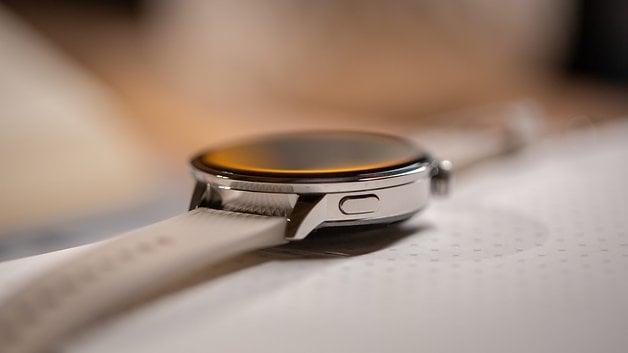Close-up of a OnePlus Watch 3 with a silver case and white strap, resting on a surface.
