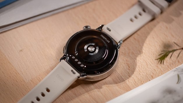 Back view of the OnePlus Watch 3 (43 mm) with a white strap on a wooden surface.