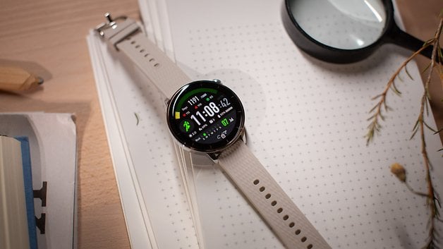 A OnePlus Watch 3 (43 mm) with a digital display showing time and fitness stats on a notebook.