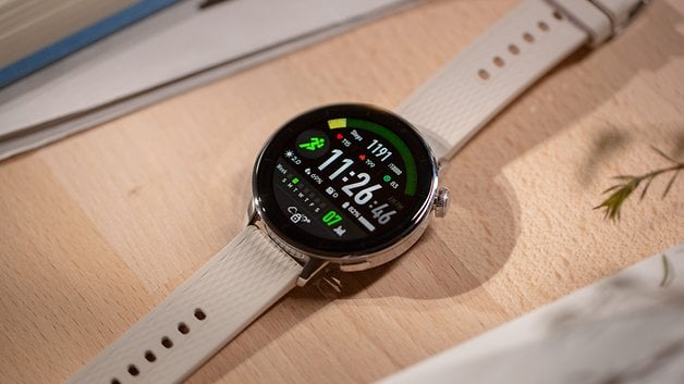 OnePlus Watch 3 with a round display showing fitness stats on a wooden surface.