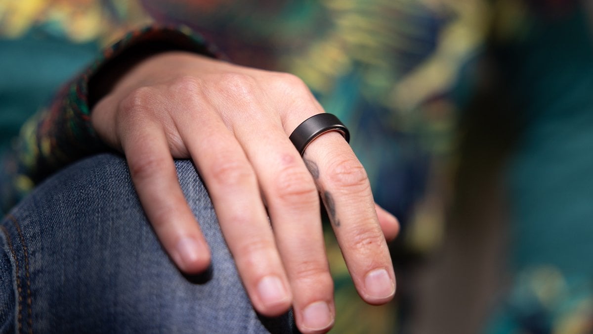 Un gros plan d'une main portant une bague Oura noire sur le doigt, reposant sur un genou.