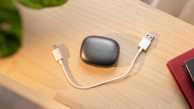 Un boîtier de charge pour Redmi Buds 6 Pro avec un câble USB sur une surface en bois.