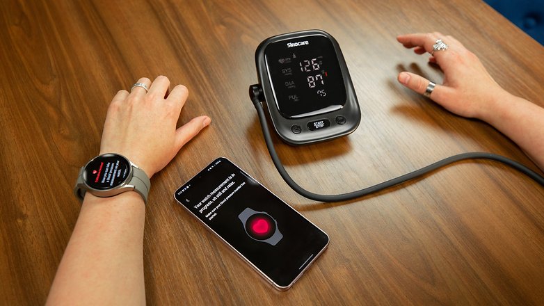 A digital Blood Pressure Monitor side by side with a Samsung Galaxy S23 and the Galaxy Watch 5 Pro