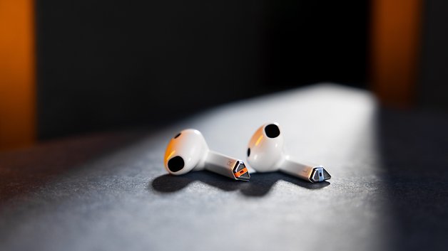 Two Samsung Galaxy Buds 3 rest on a dark surface with light casting some shadow.