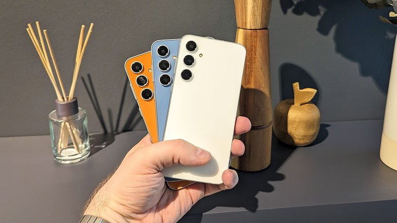 Trois Galaxy S23 FE tenus dans une main comme des cartes à jouer montrant les différents coloris: orange, bleu et blanc