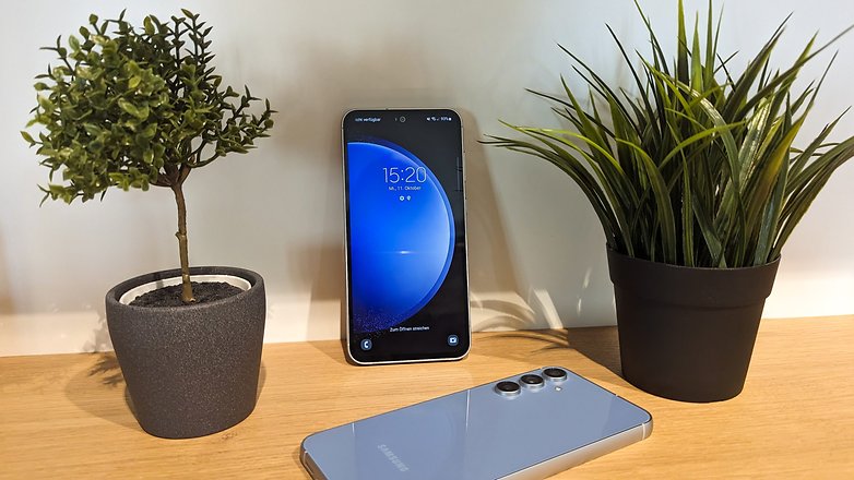 Le Samsung Galaxy S23 FE vu de côté, posé à plat face contre terre sur une table en bois entre deux plantes de bureau