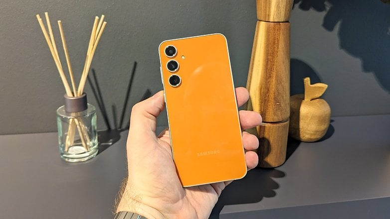 Le Samsung Galaxy S23 FR vu de dos, tenu dans une main, avec un aperçu de son coloris orange "Tangerine"