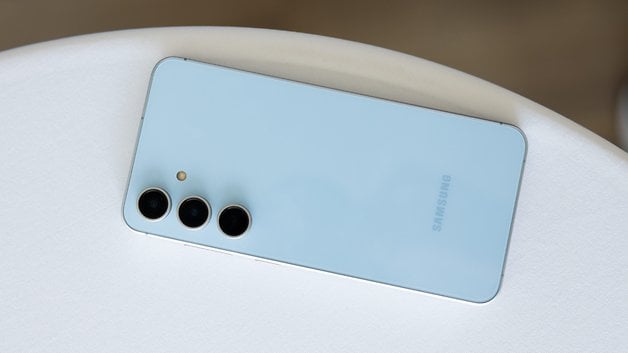 Samsung Galaxy S24 FE smartphone with three cameras on the back, placed on a white surface.