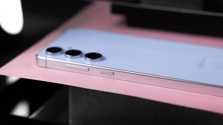 Samsung Galaxy S24 FE smartphone lying on a pink surface with three rear cameras visible.