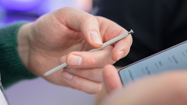 A hand holding a stylus above a smartphone screen.