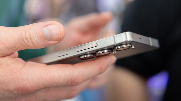 A person holding a Samsung Galaxy S25 smartphone, showing its side with buttons and camera lenses visible.