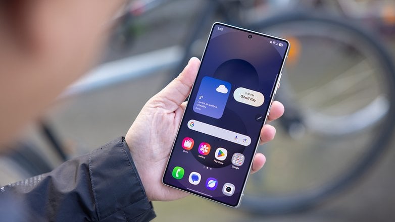 A person holding a Samsung Galaxy S25 Ultra smartphone displaying weather information and app icons.