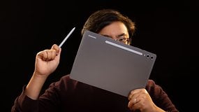 Person hält ein Samsung Galaxy Tab S10+ und einen Stylus vor einem dunklen Hintergrund.