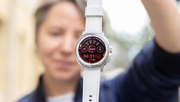 Uma pessoa segurando um Samsung Galaxy Watch 8 Classic, exibindo uma interface vermelha com hora e estatísticas de fitness.