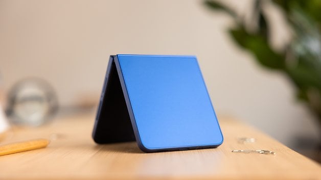 Ein blauer Samsung Galaxy Z Flip 7 Smartphone in gefaltetem Zustand auf einem Holztisch.
