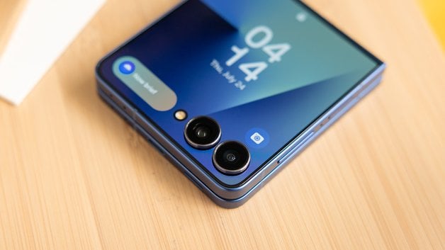 Samsung Galaxy Z Flip7 Smartphone mit Dual-Kameras und blauer Oberfläche auf einem Holzuntergrund.
