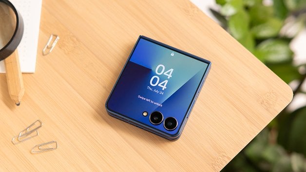 Ein Samsung Galaxy Z Flip7 Smartphone auf einer Holzoberfläche, das die Uhrzeit und das Datum zeigt.