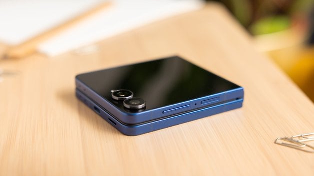 Ein Samsung Galaxy Z Flip7 Smartphone in blauer Farbe, das auf einer Holzoberfläche liegt.