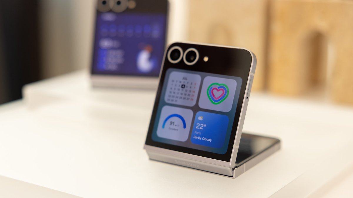Samsung Galaxy Z Flip 6 smartphone displayed on a stand with a colorful screen showing weather and calendar.