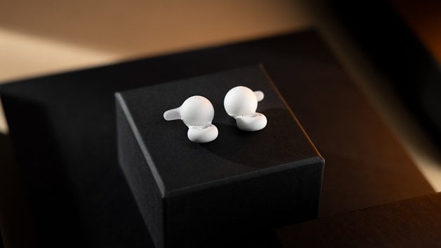 White Sony Link Buds placed on a black box with soft lighting.