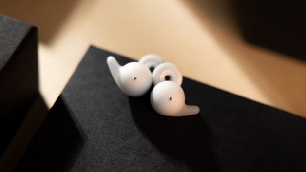 White Sony LinkBuds resting on a black surface, highlighting their unique design.