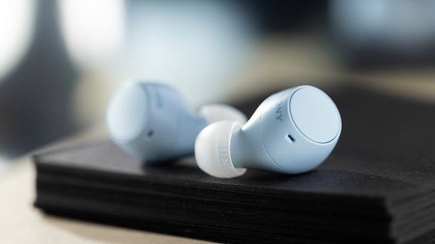 Die hellblauen Earbuds liegen auf einem Stapel schwarzer Blocks.