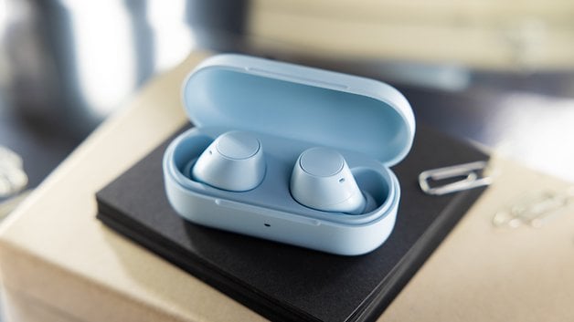 Light blue wireless earbuds in the charging case on a black notebook.