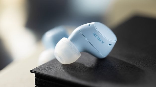 Hellblaue Sony-WF-C510-Buds liegen auf einem Stapel schwarzer Materialien.