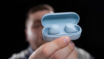 A person holding a blue charging case with wireless earbuds inside, against a dark background.