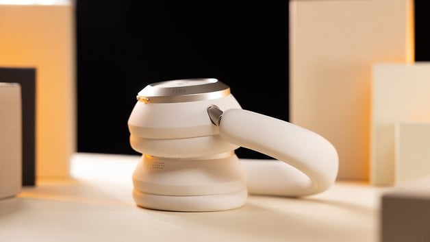 Casque audio blanc circum-aural au design élégant, posé sur une surface claire avec des formes géométriques en arrière-plan.