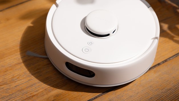 A white vacuum robot on a wooden floor, with a round design and control buttons.