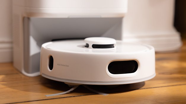 A SwitchBot K10 Pro robot vacuum cleaner with wall detection feature, on a wooden floor.