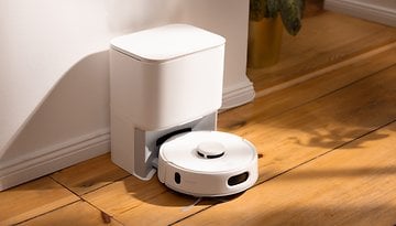 A white robotic vacuum cleaner positioned next to a charging station on wooden flooring.