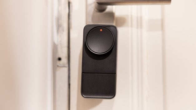 A black SwitchBot Lock Pro mounted on a door with a round button and an indicator light.