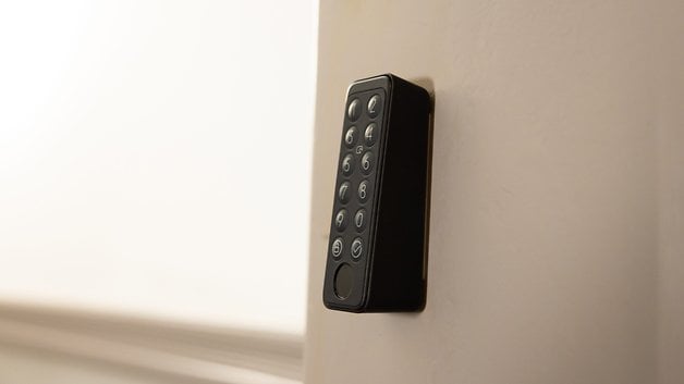 A black keypad lock mounted on a wall, with numbered keys and a round release button.