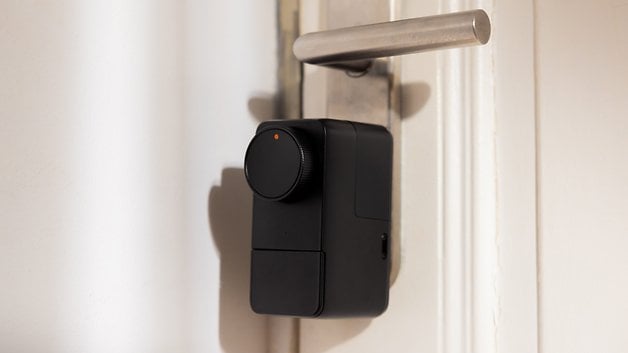 A black SwitchBot Lock Pro installed on a door with a metal handle.